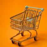 A miniature shopping cart set against a bold orange backdrop, ideal for marketing and business visuals.